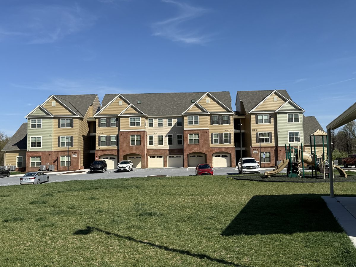 Three story Washington Landing apartment buildings with brick base and garage bays behind a lawn and playground